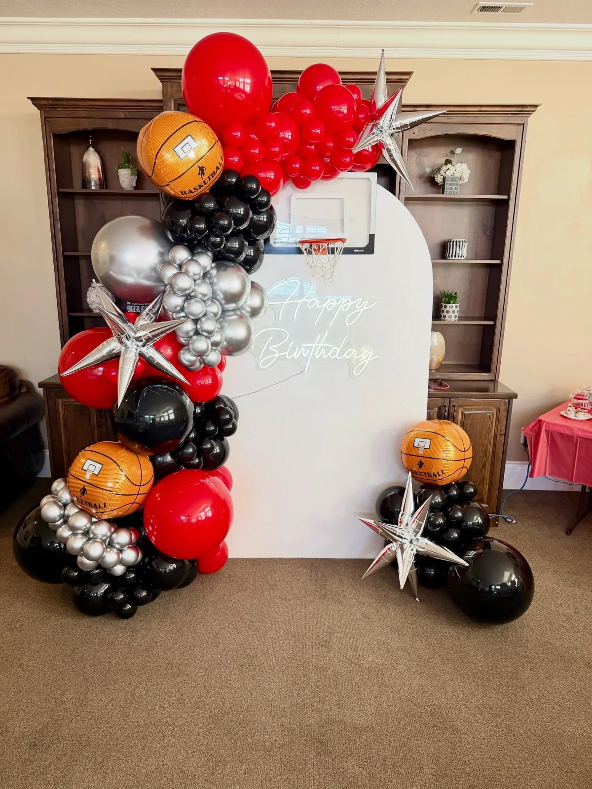 A red, black, and silver balloon garland with basketball balloons around a white arch and a Happy Birthday sign