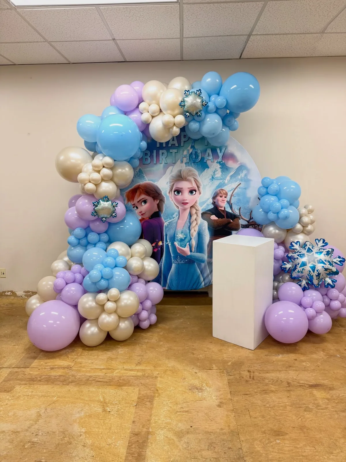 A blue, lilac, and cream balloon garland around a Frozen-themed birthday backdrop