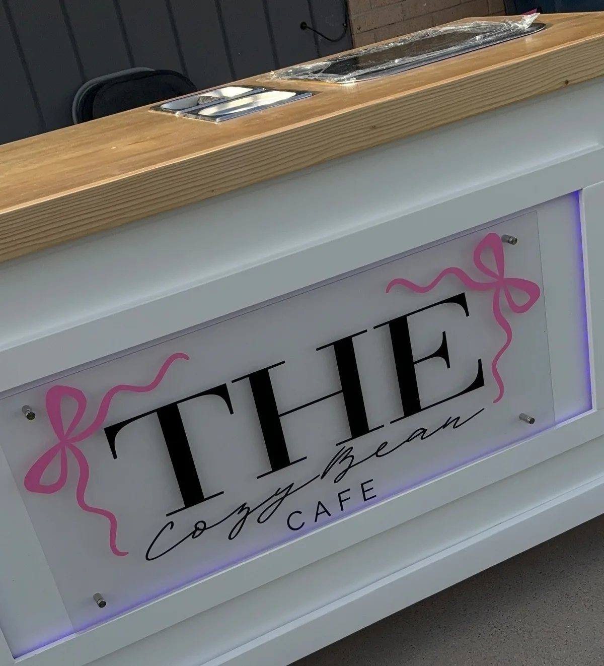 The white Cozy Bean Cafe cart with a wooden top and a pink bow sign