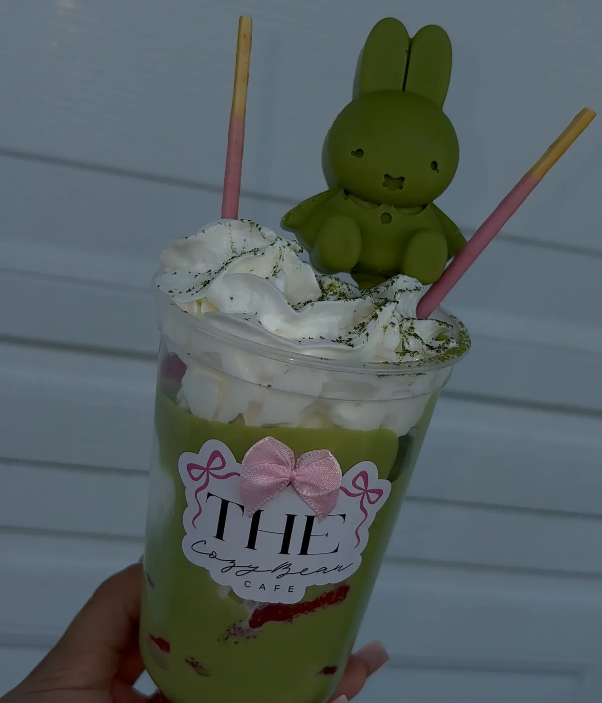 A matcha drink with whipped cream, pink wafer sticks, and a green chocolate bunny