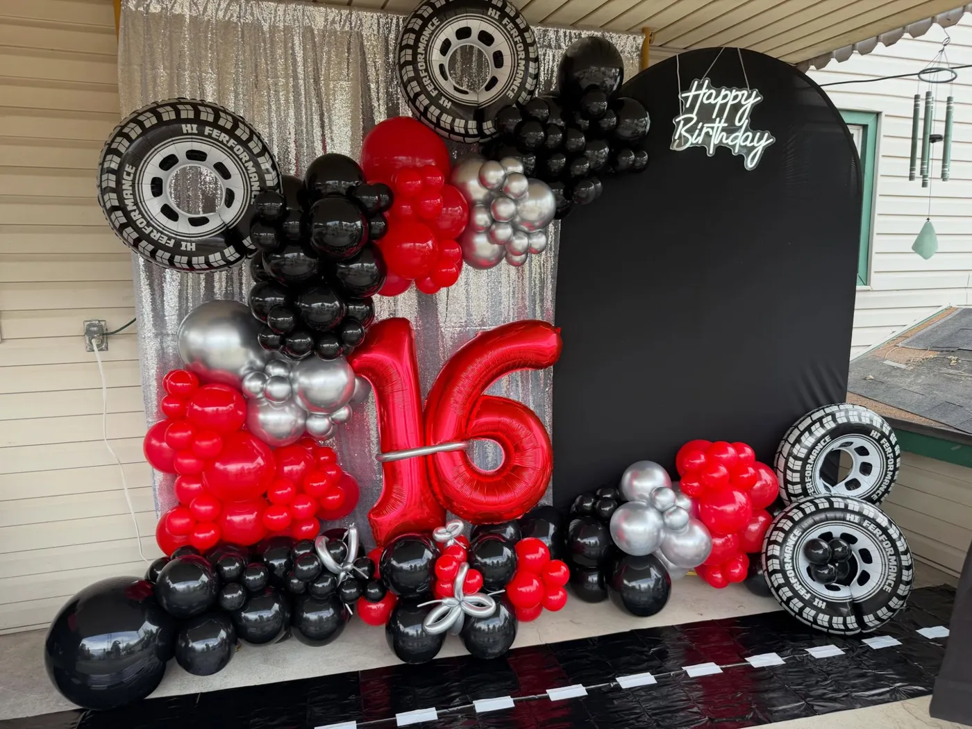 A red, black, and silver balloon arrangement with a number 16 and a Happy Birthday sign