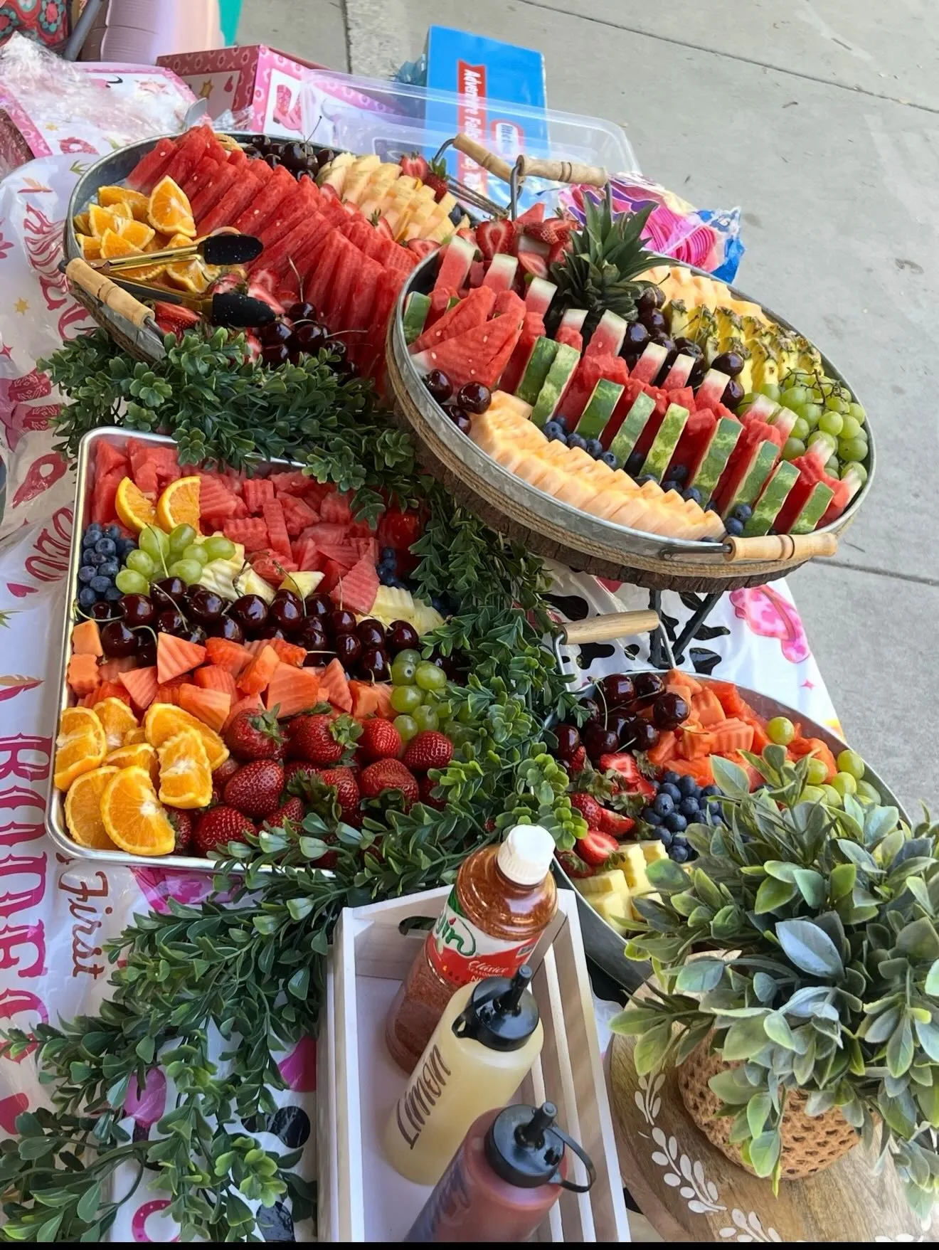 Trays of fresh watermelon, cantaloupe, berries, and grapes with greenery