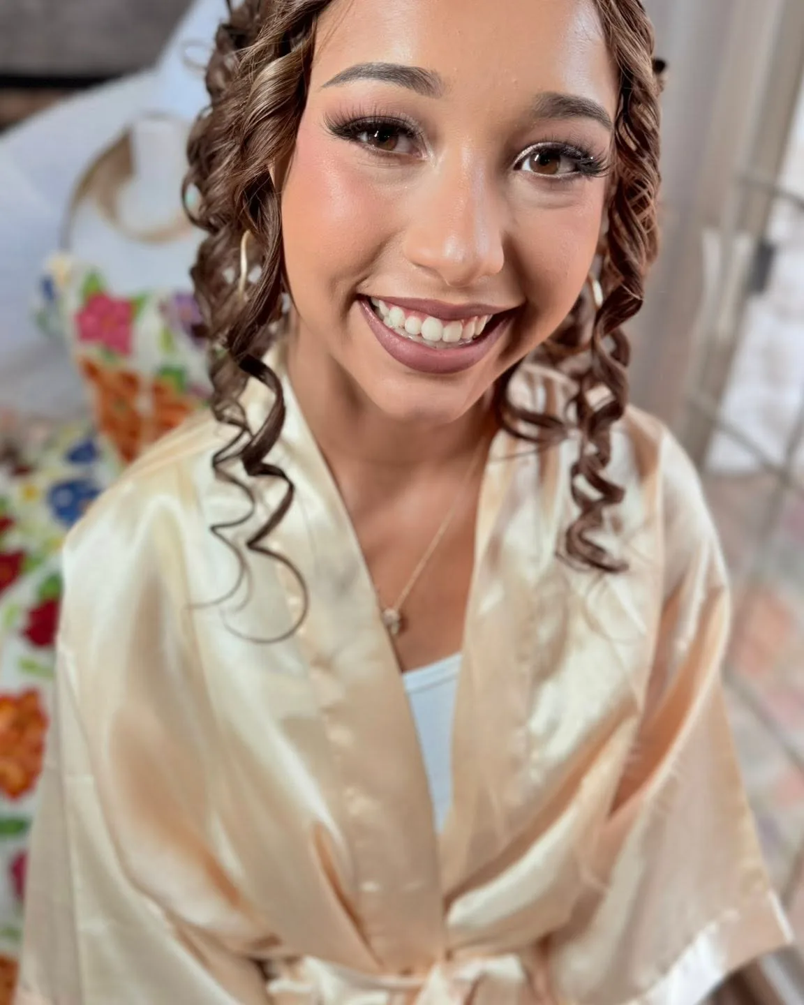 A smiling client in a champagne robe with glowing makeup and long curls
