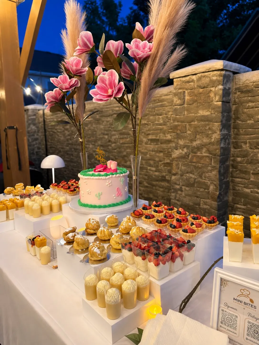 A Mini Bites dessert table with a pink cake, fruit tarts, and cream puffs