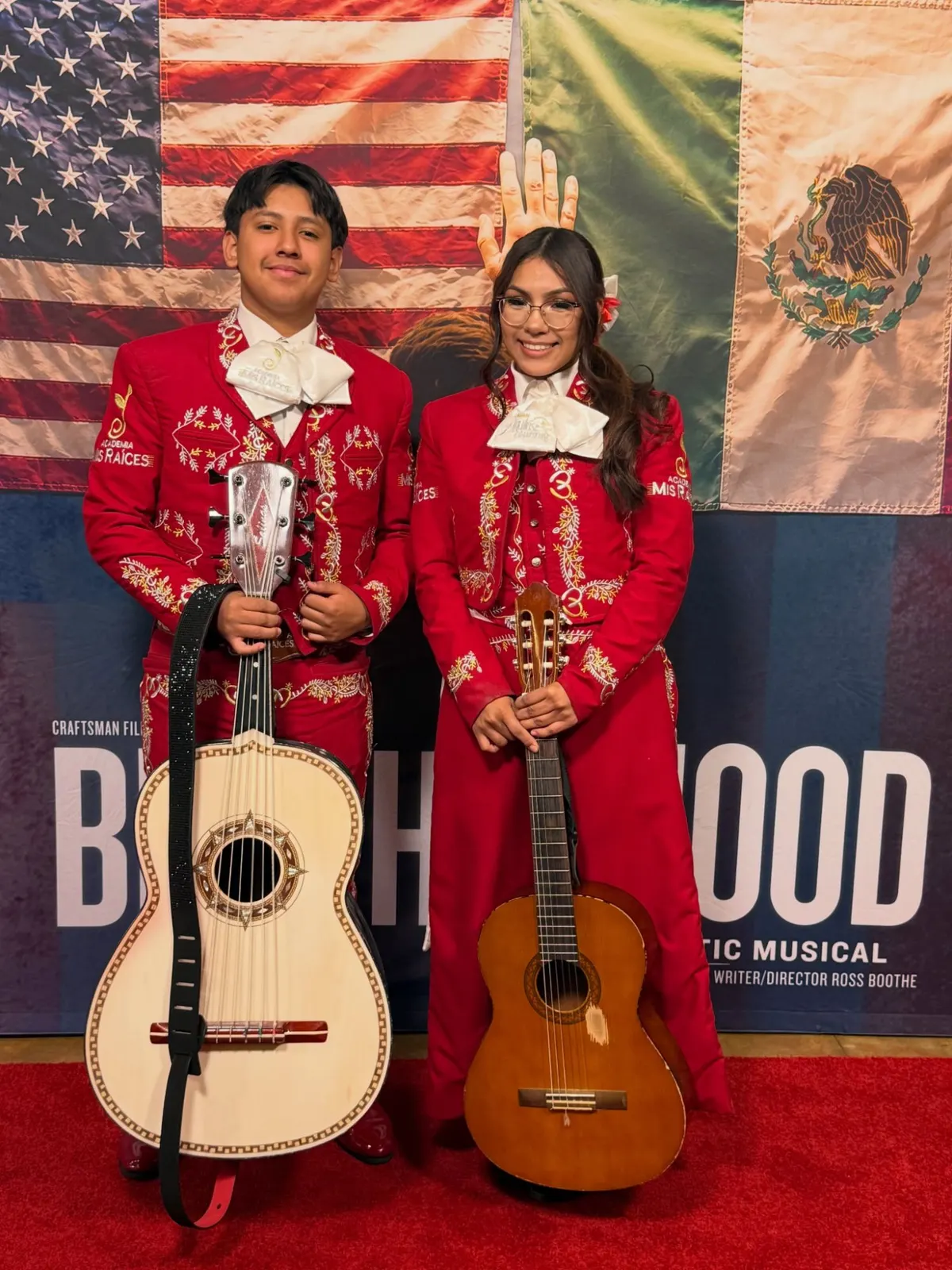 Two Academia Mis Raíces students in mariachi trajes with a guitarrón and a guitar