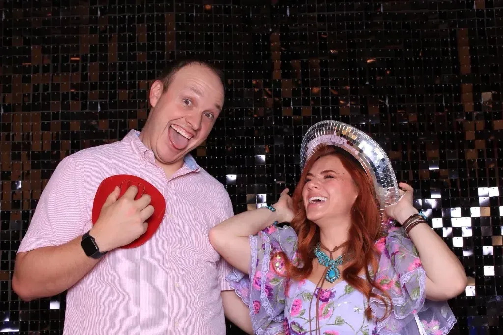 A couple laughing under a disco ball cowboy hat