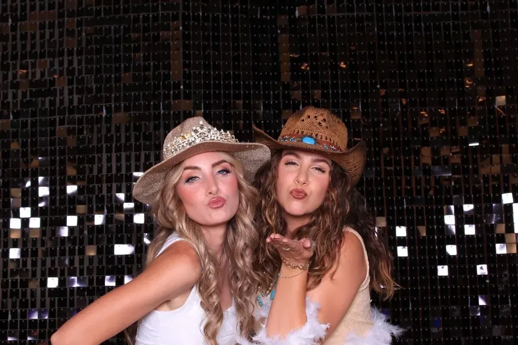Two guests in glam cowboy hats blowing kisses