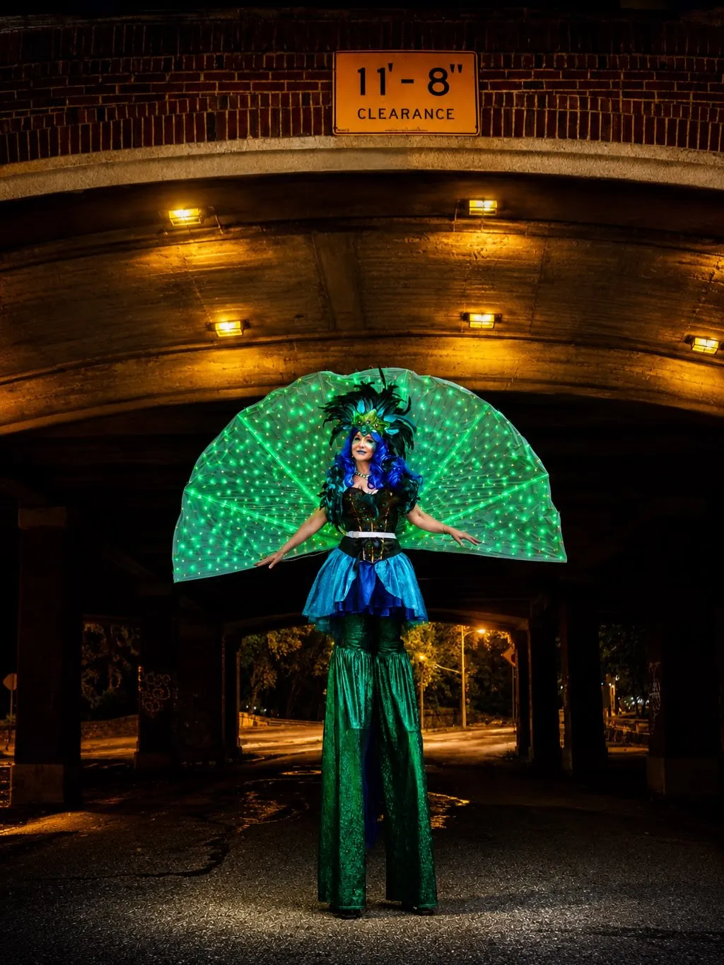 A stilt walker with a glowing green LED peacock fan
