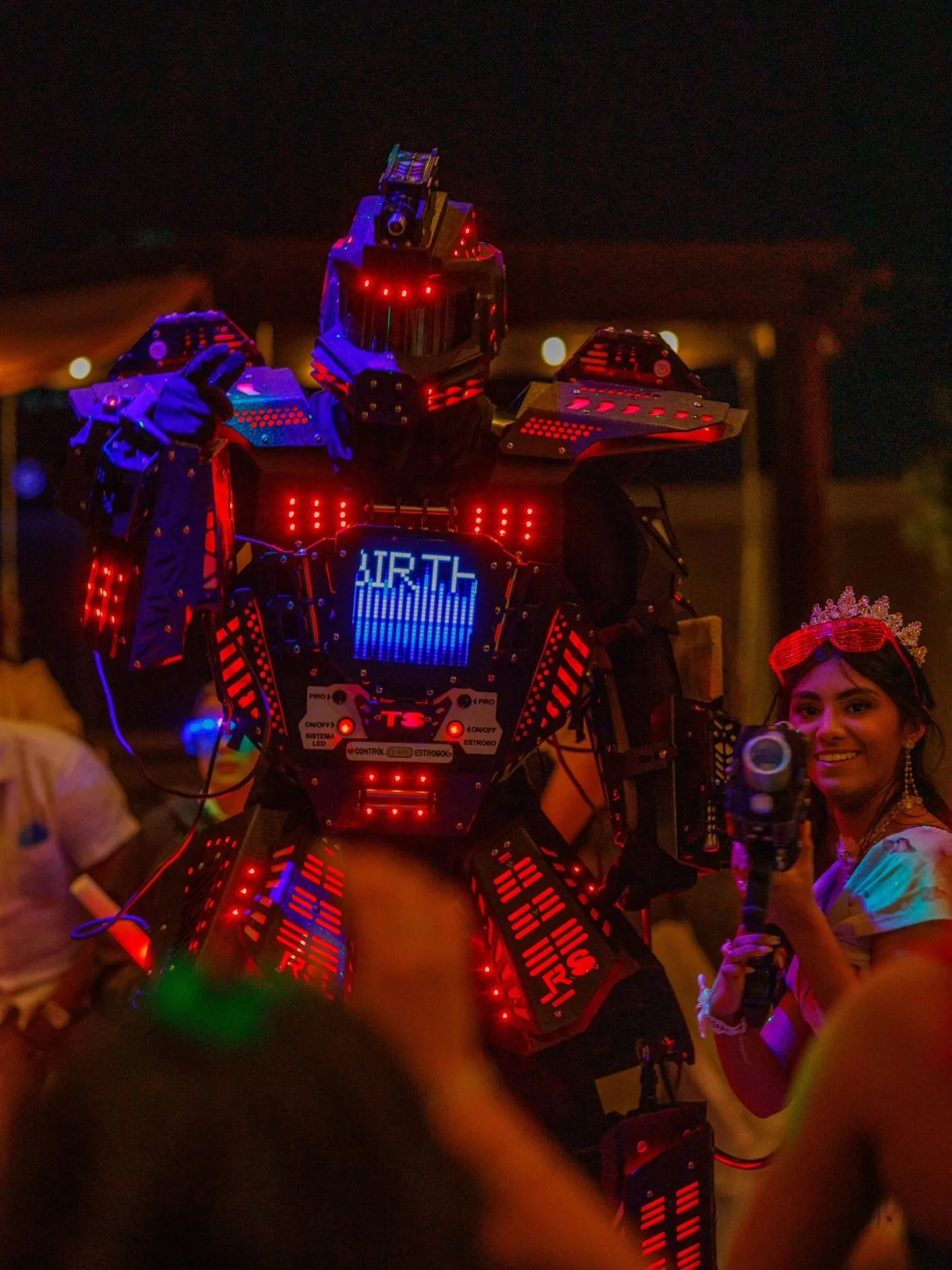 A robot with a glowing chest screen next to a smiling quinceañera