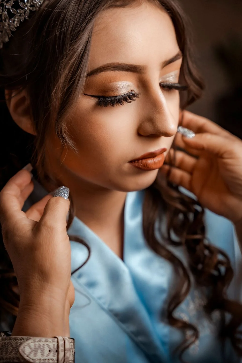 Diamond earrings being placed on a young woman with glamorous makeup and curls