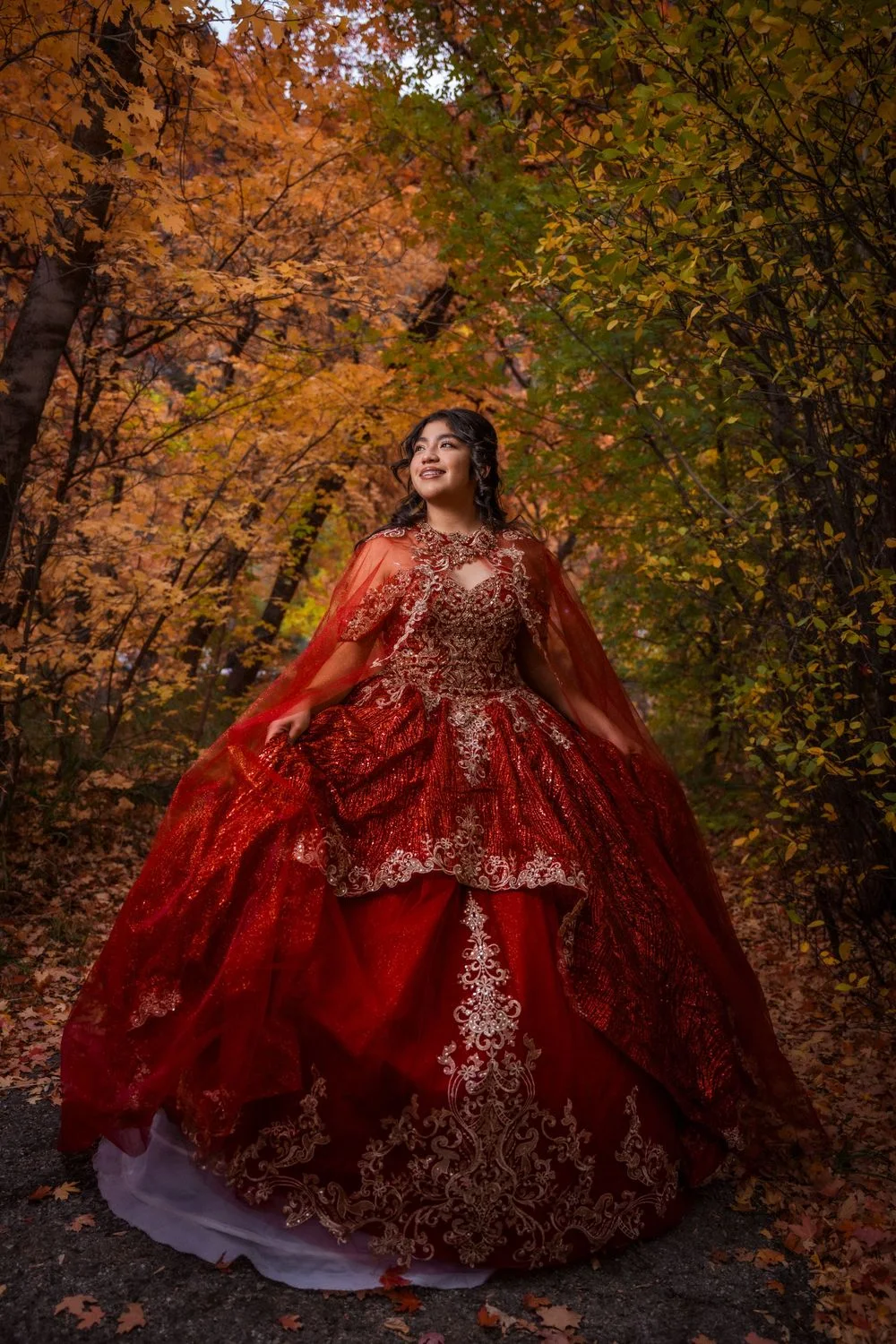 A young woman in a red sequined gown with a cape in an autumn forest