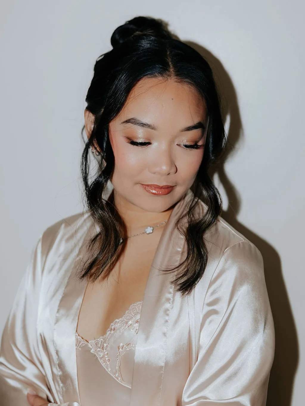 A client in a champagne satin robe with glowing skin, soft eyeshadow, and a half-up knot