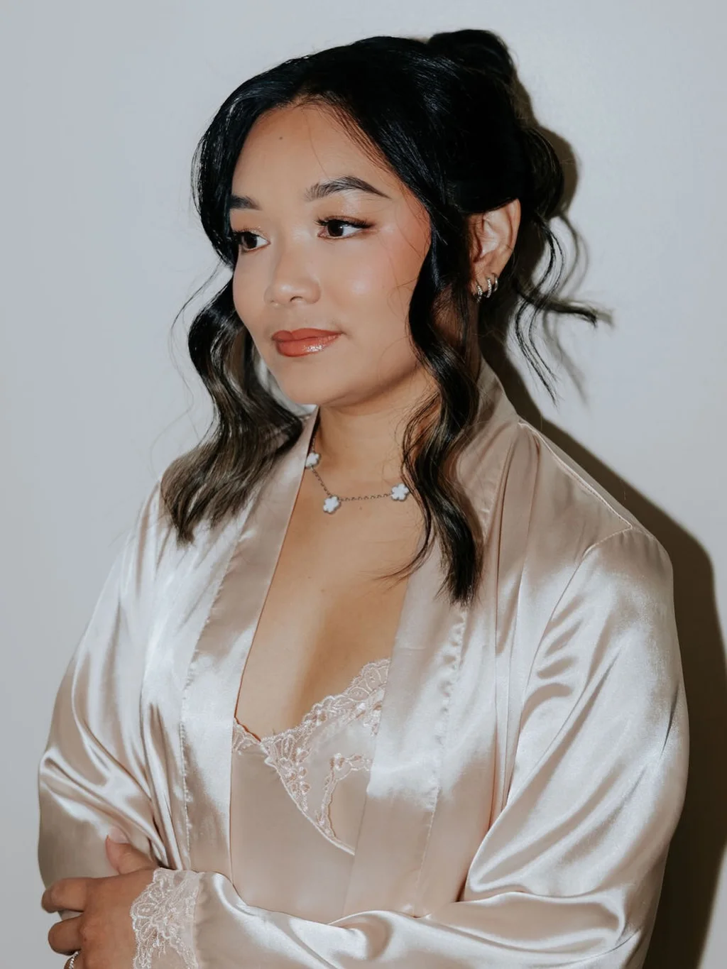 A client in a satin robe with soft waves, a half-up knot, and warm glowing makeup