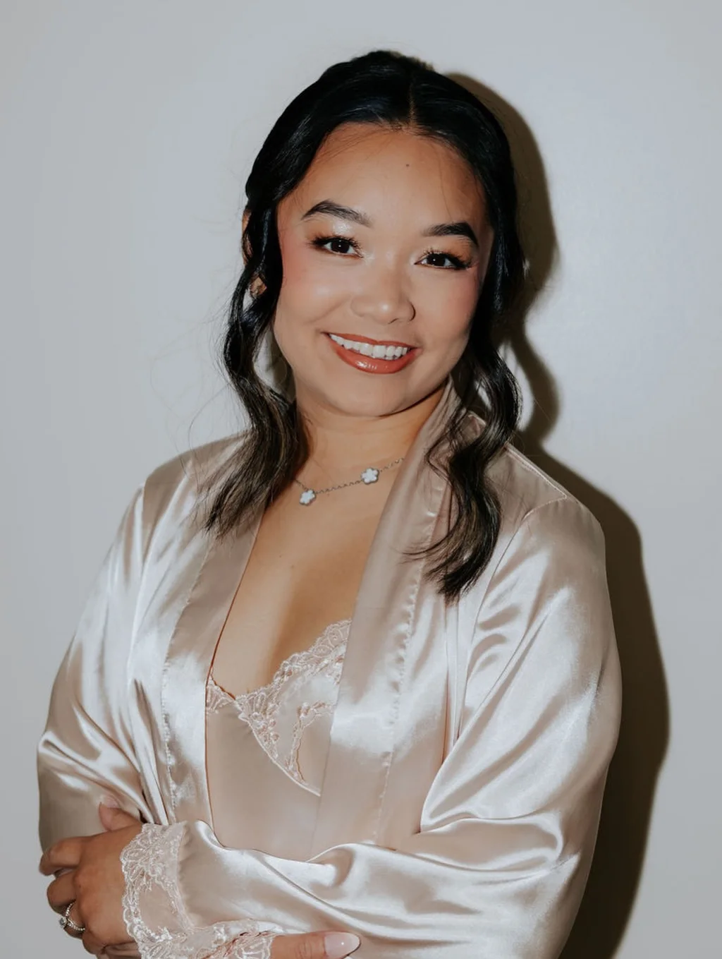 A smiling client in a satin robe with glowing makeup and soft waves